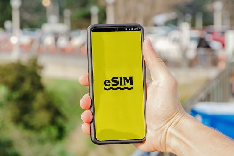 A person holds a smartphone featuring an eSIM display against an outdoor urban backdrop.