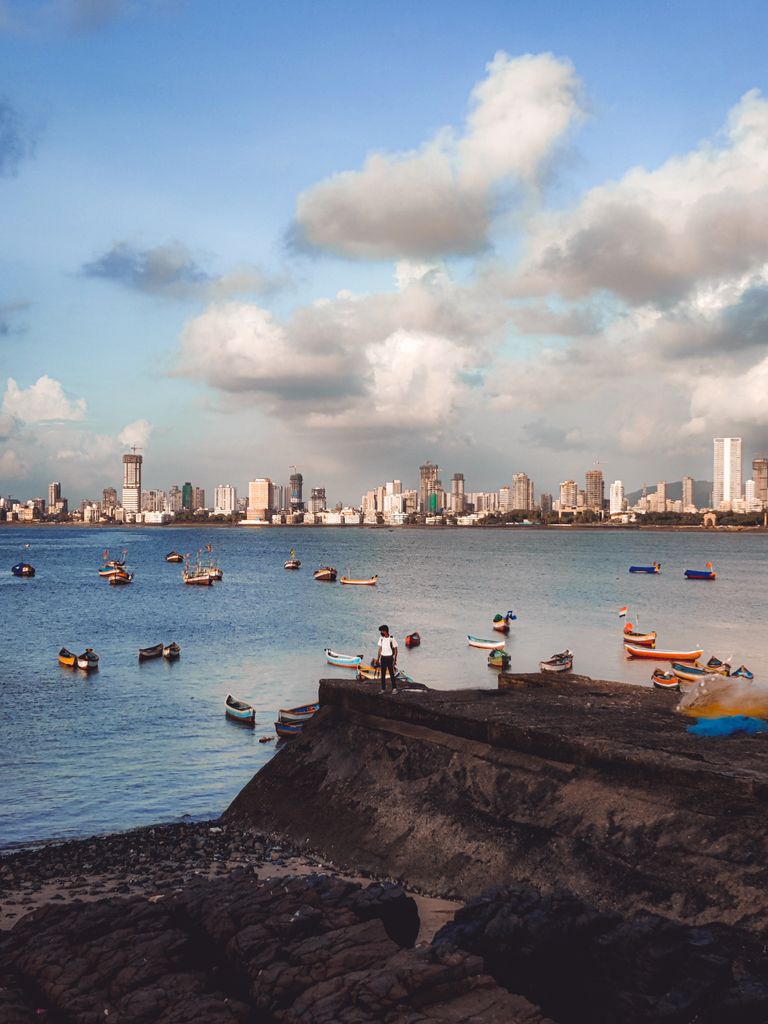 Boats scattered on a peaceful bay with a bustling city skyline and fluffy clouds above.
