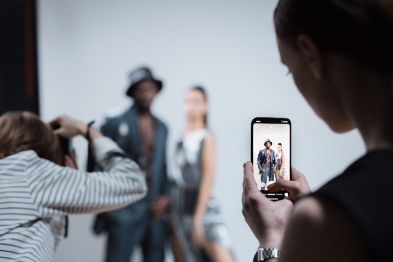 Fashion models being photographed in a professional studio setting with smartphone capture.